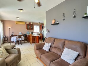 Ein Wohnzimmer mit braunem Ledersofa, einem Essbereich mit Tisch und Stühlen sowie einer Küchenzeile mit Schränken und Arbeitsfläche.