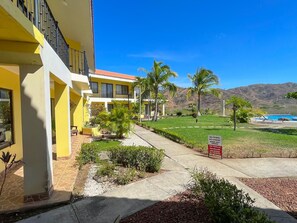 A hotel with a yellow facade, a pool, and a clear view of the mountains. - Colinas Dolce Vita 8017 – 2 Bedroom, 2 Bathroom Condo (Playas del Coco)