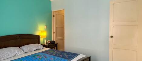 Une chambre à coucher avec un lit, une table de chevet, une lampe, un ventilateur de plafond et une porte.