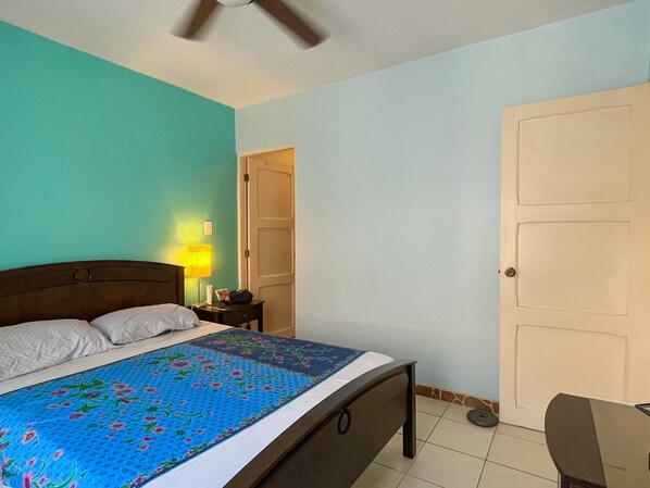 A bedroom with a bed, a nightstand, a lamp, a ceiling fan, and a door.