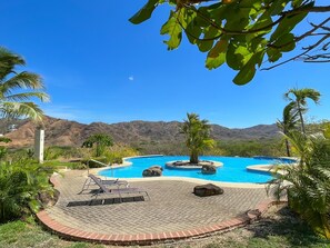 Ein Pool mit gewölbter Kante, umgeben von Palmen und einer Bergkulisse.