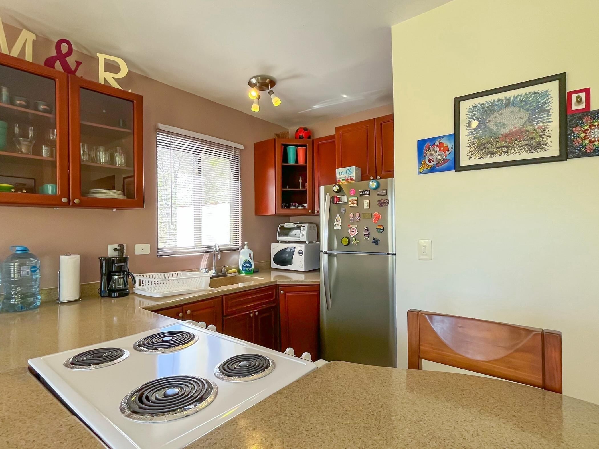 A kitchen with a stove, refrigerator, and microwave. There are wooden cabinets and a window with blinds.