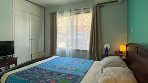 Ett hotellrum med en säng, en TV, en luftkonditionering, en takfläkt och ett fönster med gardiner.