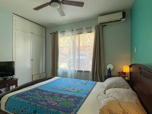 Ein Hotelzimmer mit Bett, Fernseher, Klimaanlage, Deckenventilator und einem Fenster mit Vorhängen.