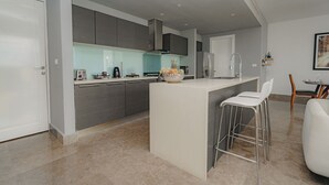 A modern kitchen with grey cabinets, a white countertop, and a central island with bar stools.