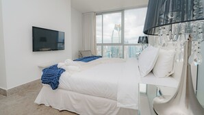 A modern hotel room with a large bed, a flat-screen TV, a city view, and a chandelier.