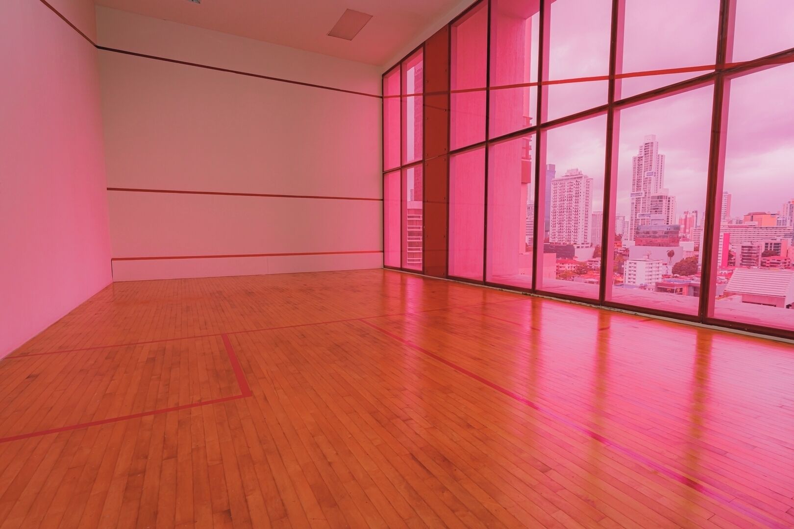 A spacious room with a wooden floor and large windows offering a city view.