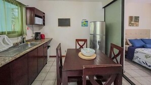 A compact kitchen with a dining table, chairs, a refrigerator, and a microwave.
