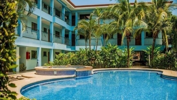 A swimming pool surrounded by lush greenery and a multi-story building with balconies.