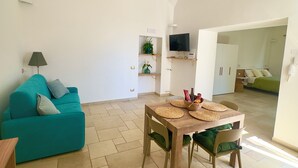 Uma sala de estar com um sofá azul-turquesa, uma mesa de jantar de madeira com jogos americanos trançados e uma TV fixada na parede.