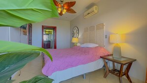 A bedroom with a bed, bedside lamps, a ceiling fan, an air conditioning unit, and a door leading to another room. - Colinas Turquesa L4C Spectacular Ocean-View Vacation Rental (Playas del Coco)