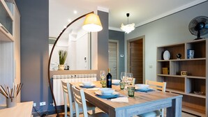 Un coin repas avec une table en bois dressée pour quatre personnes, un lampadaire et une bibliothèque contenant divers objets.