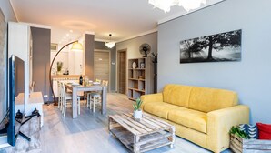 Un salon moderne avec un canapé jaune, un coin repas avec une table et des chaises, une table basse agrémentée d’une plante et une bibliothèque.
