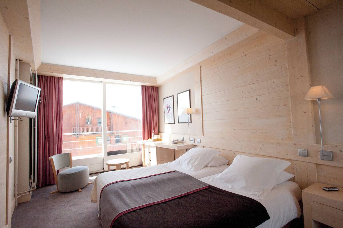 Hotellihuone, jossa on sänky, työpöytä, tuoli, televisio ja ikkuna, jossa on verhot.