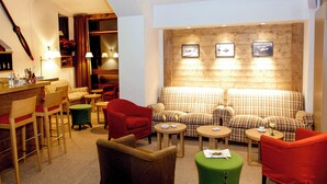A cozy hotel lobby with a bar area, checkered sofas, and a wooden accent wall with framed pictures. - Hôtel Le Ski d'Or (Tignes)