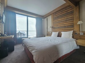 Habitación de hotel con una cama grande, cabecero de madera, un escritorio con teléfono y vista por la ventana.