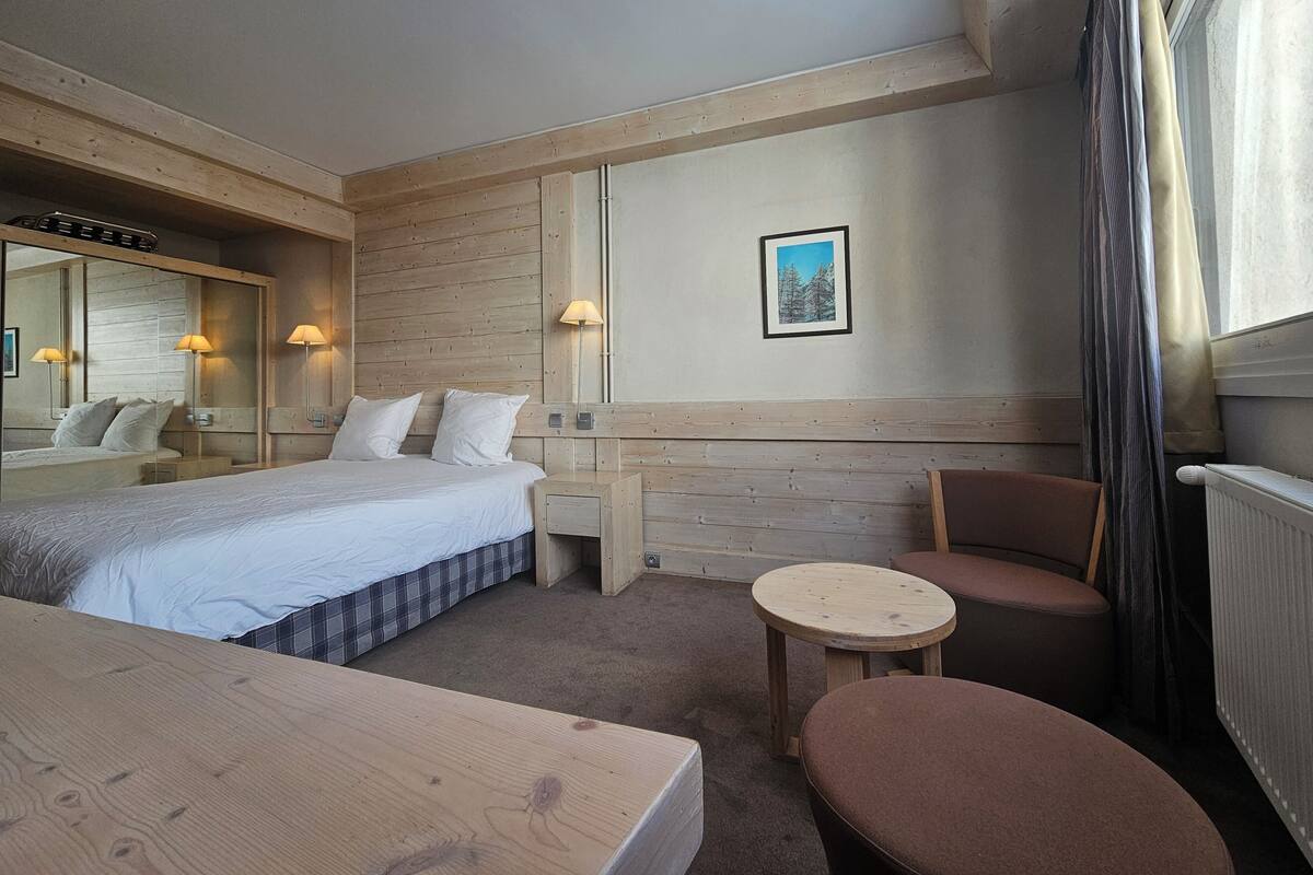 Hotellihuone, jossa on sänky, pieni pöytä, tuoli, peili ja taulu seinällä.