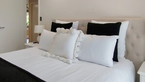 A neatly made bed with white and black pillows, a white bedspread, and a white nightstand with a lamp.