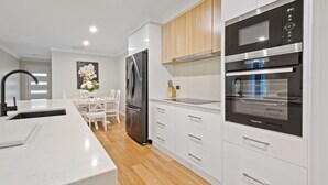 A modern kitchen with white cabinetry, a stainless steel refrigerator, a double oven, and a wooden countertop.