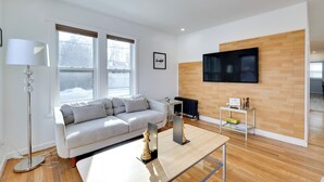En moderne stue med en hvid sofa, et sofabord, en gulvlampe og et fjernsyn monteret på en trævæg.