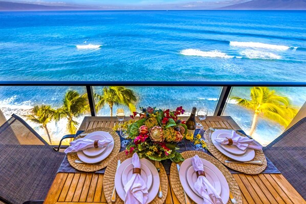 A table set for three with a view of the ocean and palm trees.