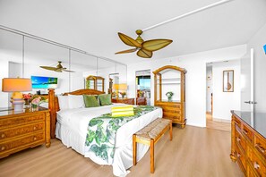 Ein helles Schlafzimmer mit einem großen Bett, Holzmöbeln, einem Deckenventilator und einem großen Spiegel.