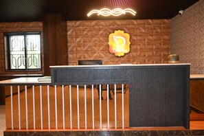 A hotel reception desk with a wooden panel wall and a logo sign. - Hotel Dwaraka (Bengaluru)