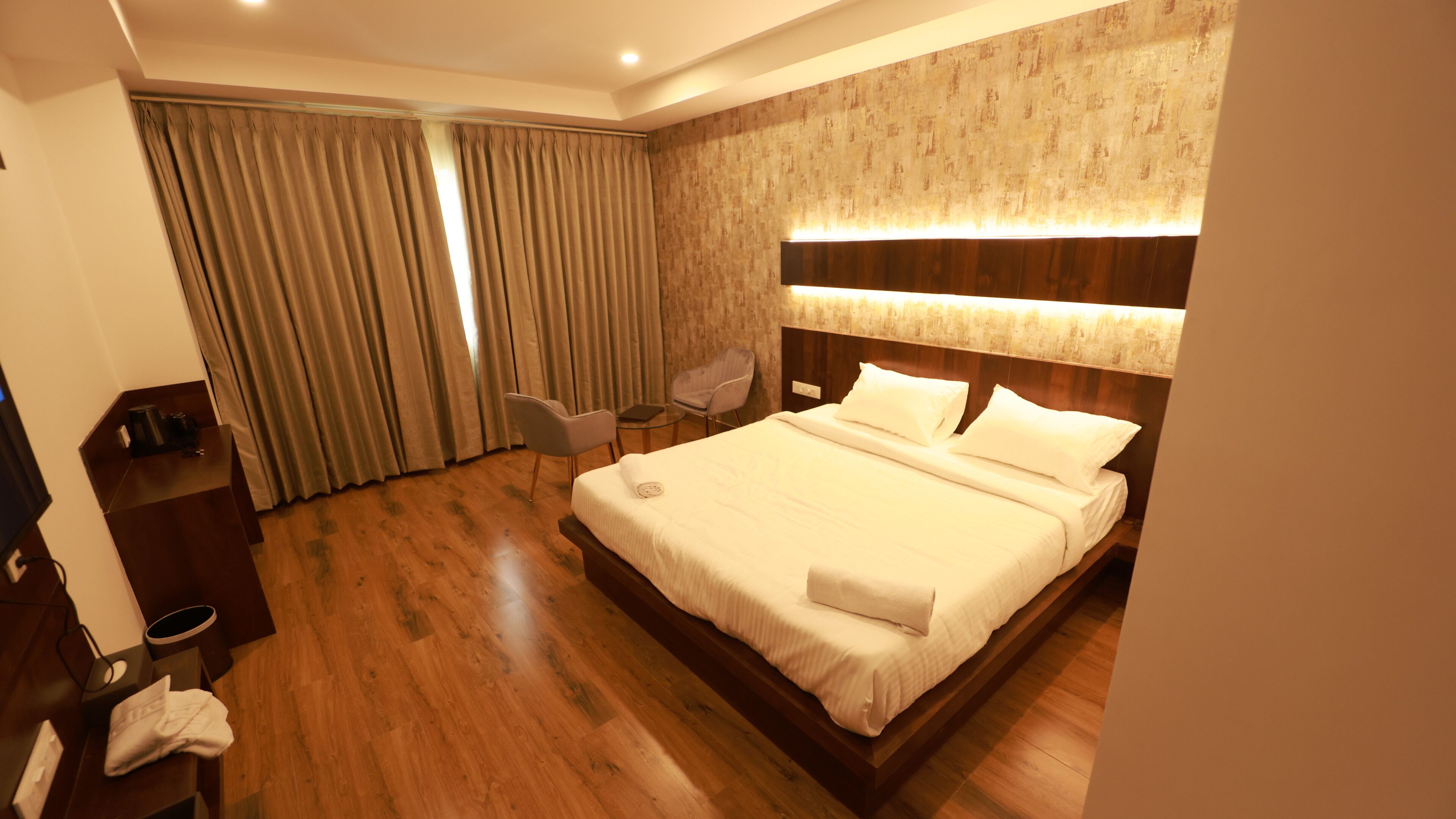 A hotel room with a large bed, a desk with a chair, a small table, and a sofa.