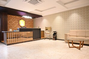 A reception area with a wooden reception desk, a sofa, and a glass table. - Hotel Dwaraka (Bengaluru)