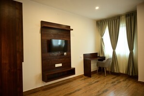 A room with a wooden entertainment unit, a flat-screen TV, a desk, and a chair. - Hotel Dwaraka (Bengaluru)