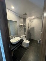A modern bathroom with a large mirror, a white sink, a toilet, and a shower area.
