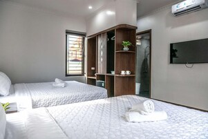A hotel room with two beds, a wardrobe, a TV, and a window with bars.