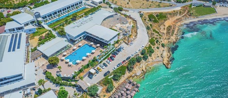 Ett flygbildsbild av ett semesterområde med en swimmingpool, sittplatser vid stranden och en stor byggnad med skylten "Spingola Hotel Resort".