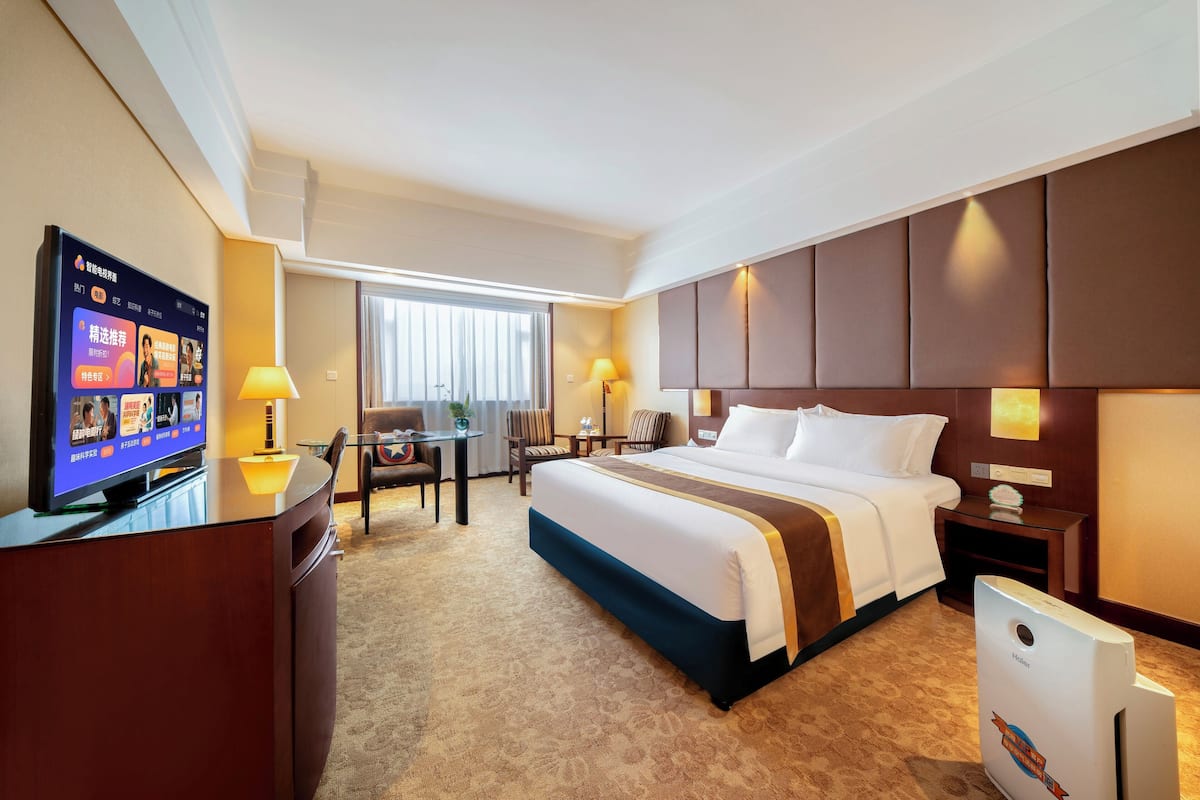A hotel room with a large bed, a desk with a computer, a television, and a minibar.