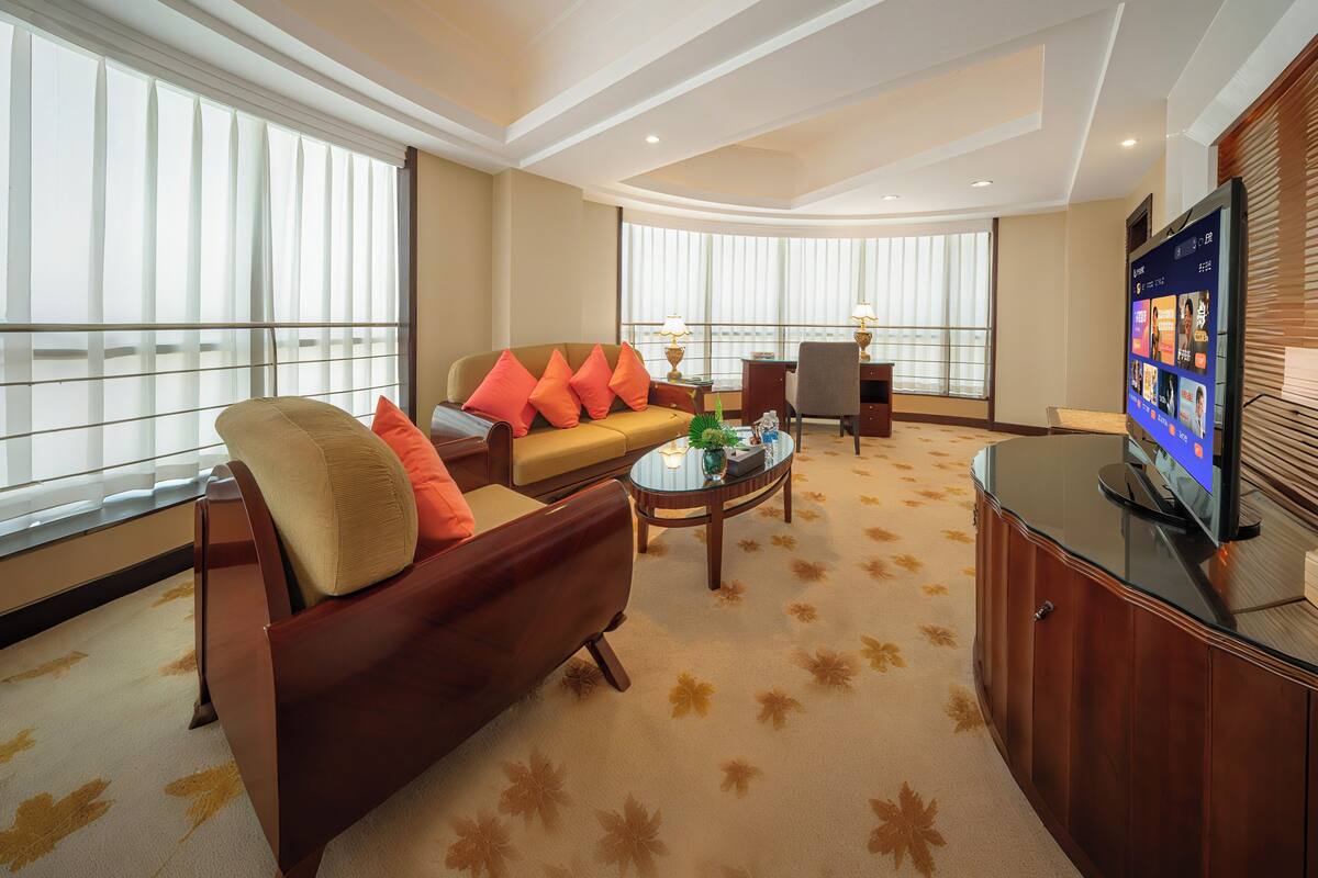 A modern hotel room with a sofa, armchair, and a flat-screen TV on a stand.