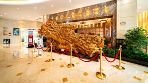 A lobby with a large golden sculpture, a reception desk, and a plant.