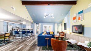 A modern living room with a blue sofa, orange armchair, and a TV mounted on the wall. - The Sunburst: Sleeps 18! Basketball & Heated Pool (San Antonio)