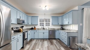 A modern kitchen with light blue cabinets, stainless steel appliances, and a marble countertop. - The Sunburst: Sleeps 18! Basketball & Heated Pool (San Antonio)