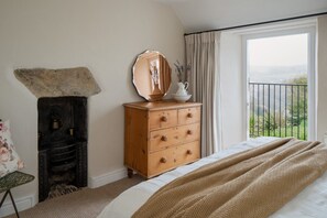 Un dormitorio con cama, cómoda, espejo, chimenea y vistas al exterior.
