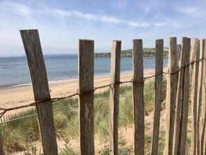 A wooden fence with barbed wire, overlooking a beach with sand and grass.