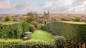 A well-maintained garden with a hedge maze, a table and chairs, and a distant view of a historic tower.