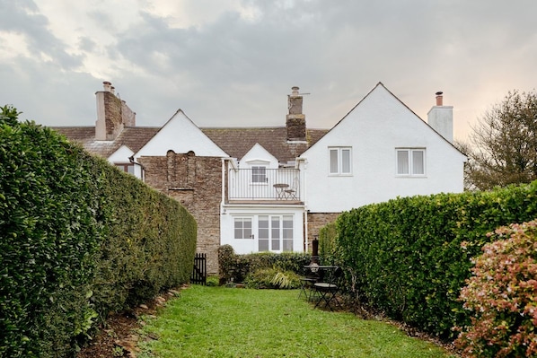 A two-story house with a white exterior, a visible balcony, and a well-maintained garden.
