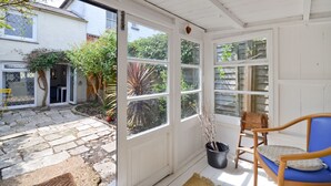 Eine überdachte Terrasse mit Steinböden, einem Holzstuhl und einem Blumentopf.