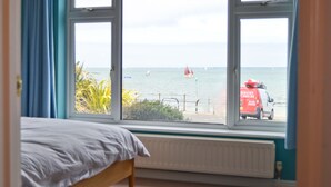 A bedroom with a large window overlooking a beach. - Princes Esplanade (Gurnard)