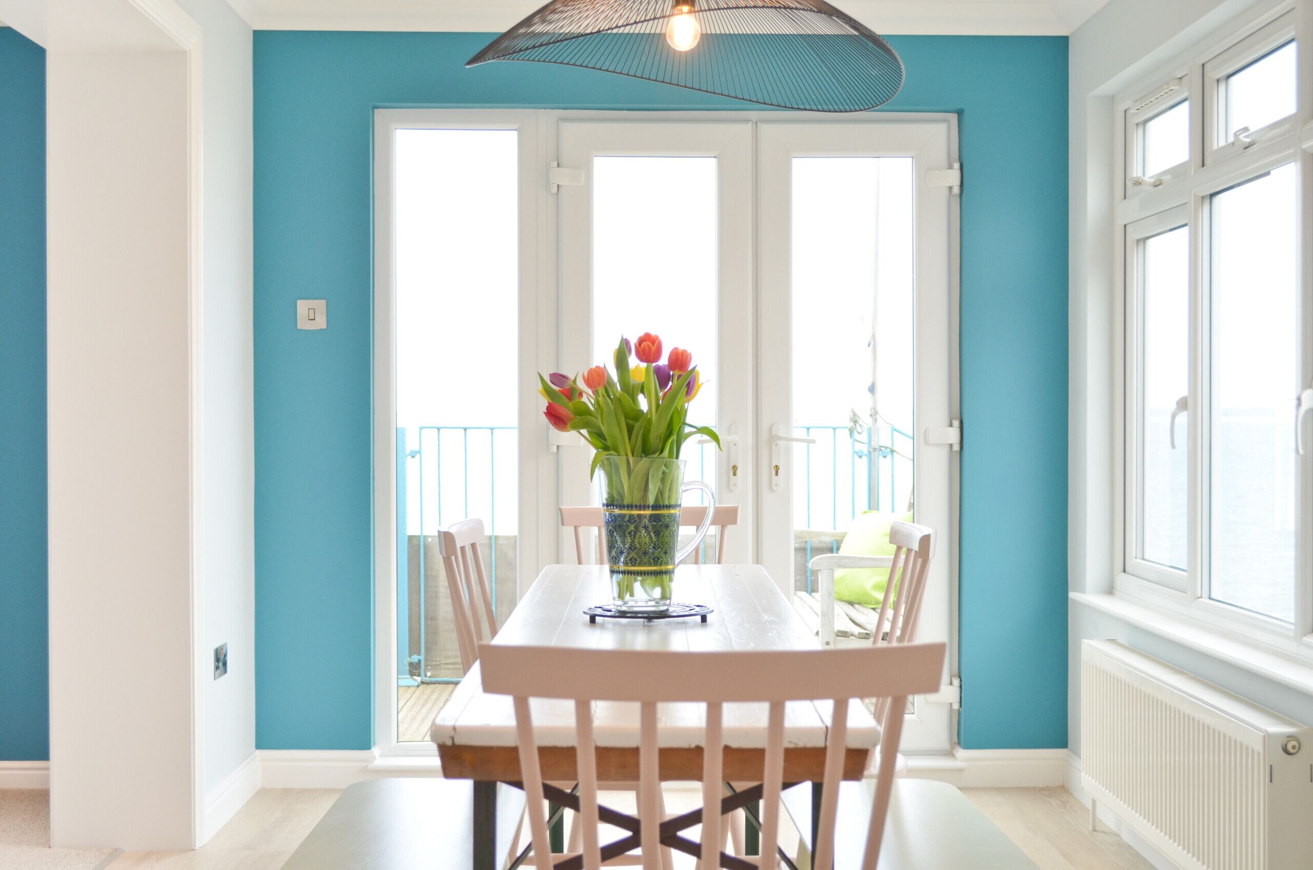 A dining area with a white table and chairs, a vase with flowers, and a view through a glass door.