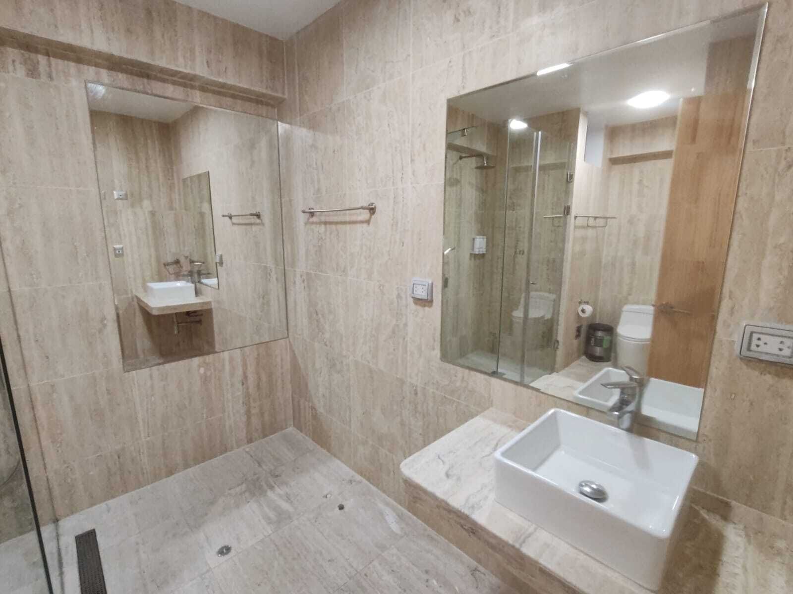 A modern bathroom with a glass-enclosed shower, a large mirror, and a marble-tiled floor.