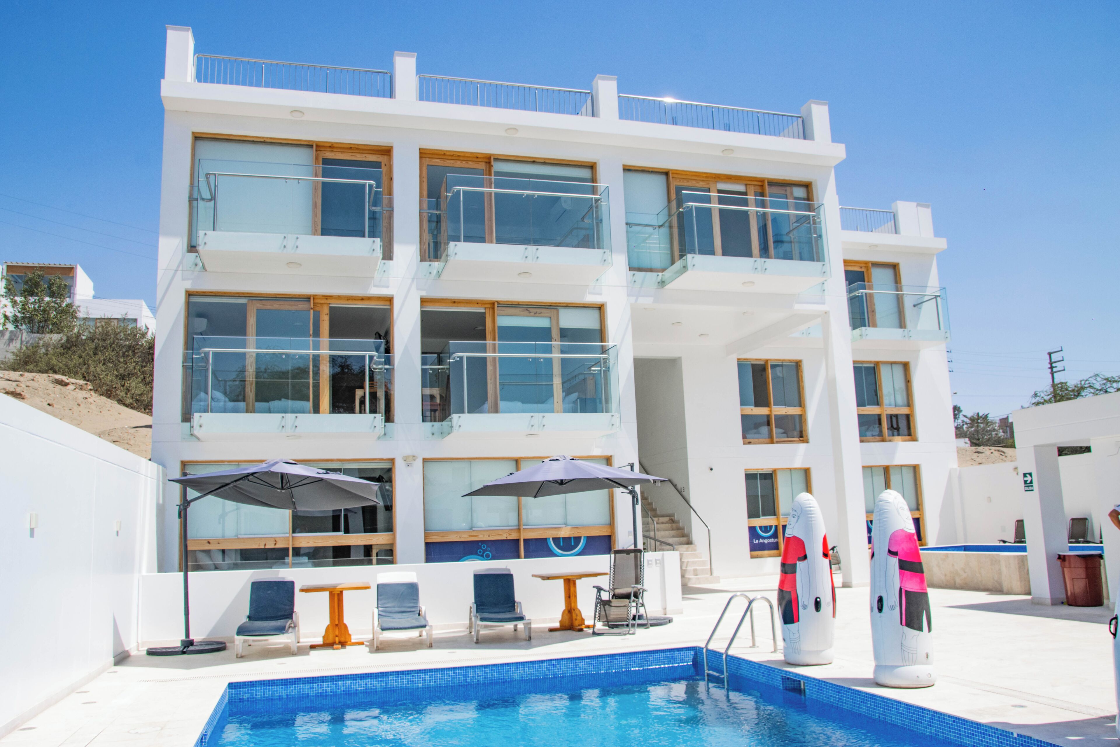 A modern hotel with a pool area, multiple balconies, and sun loungers.