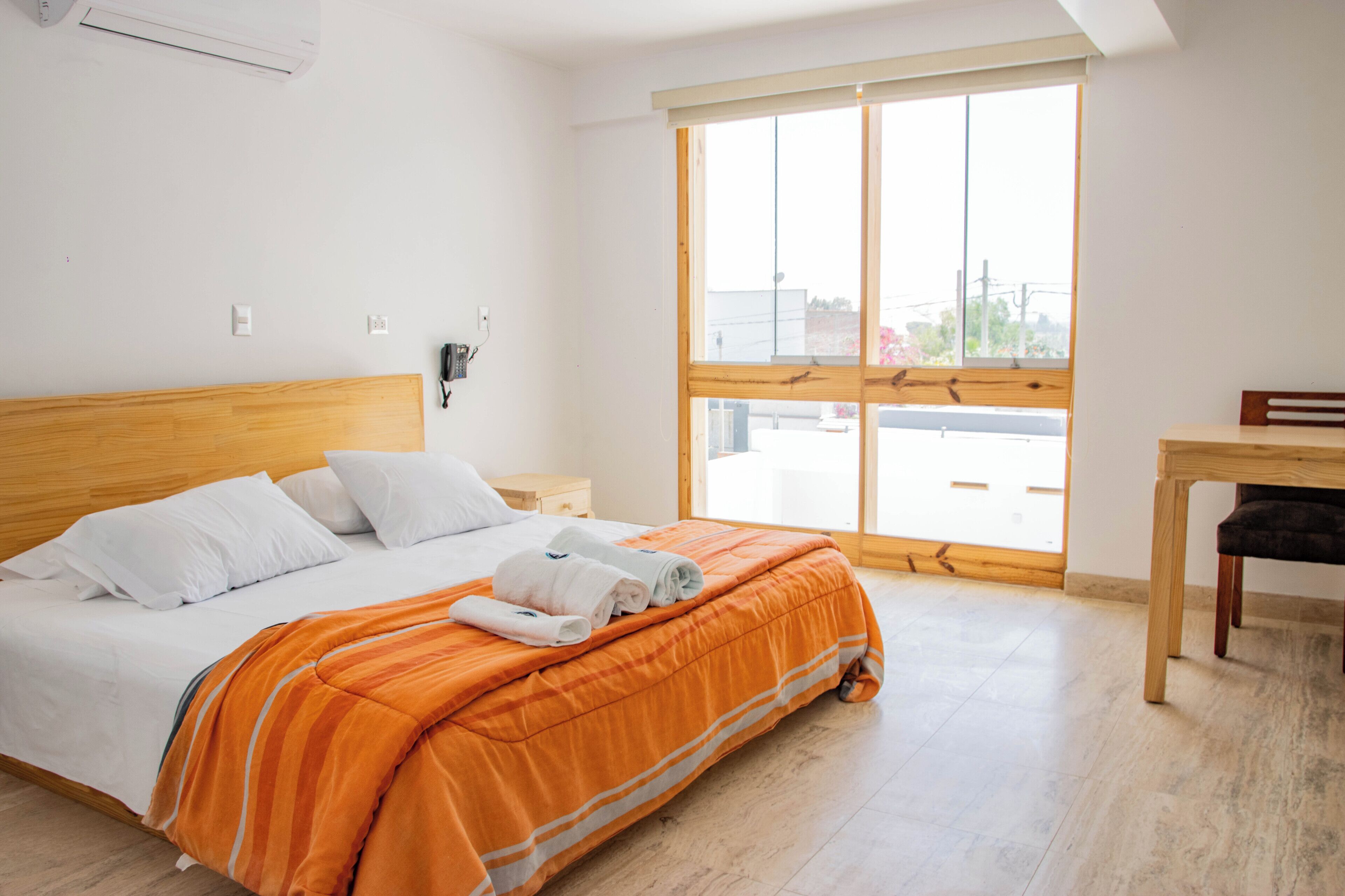 Una habitación de hotel con una cama, cabecera de madera, una ventana con persianas, un escritorio y una silla.