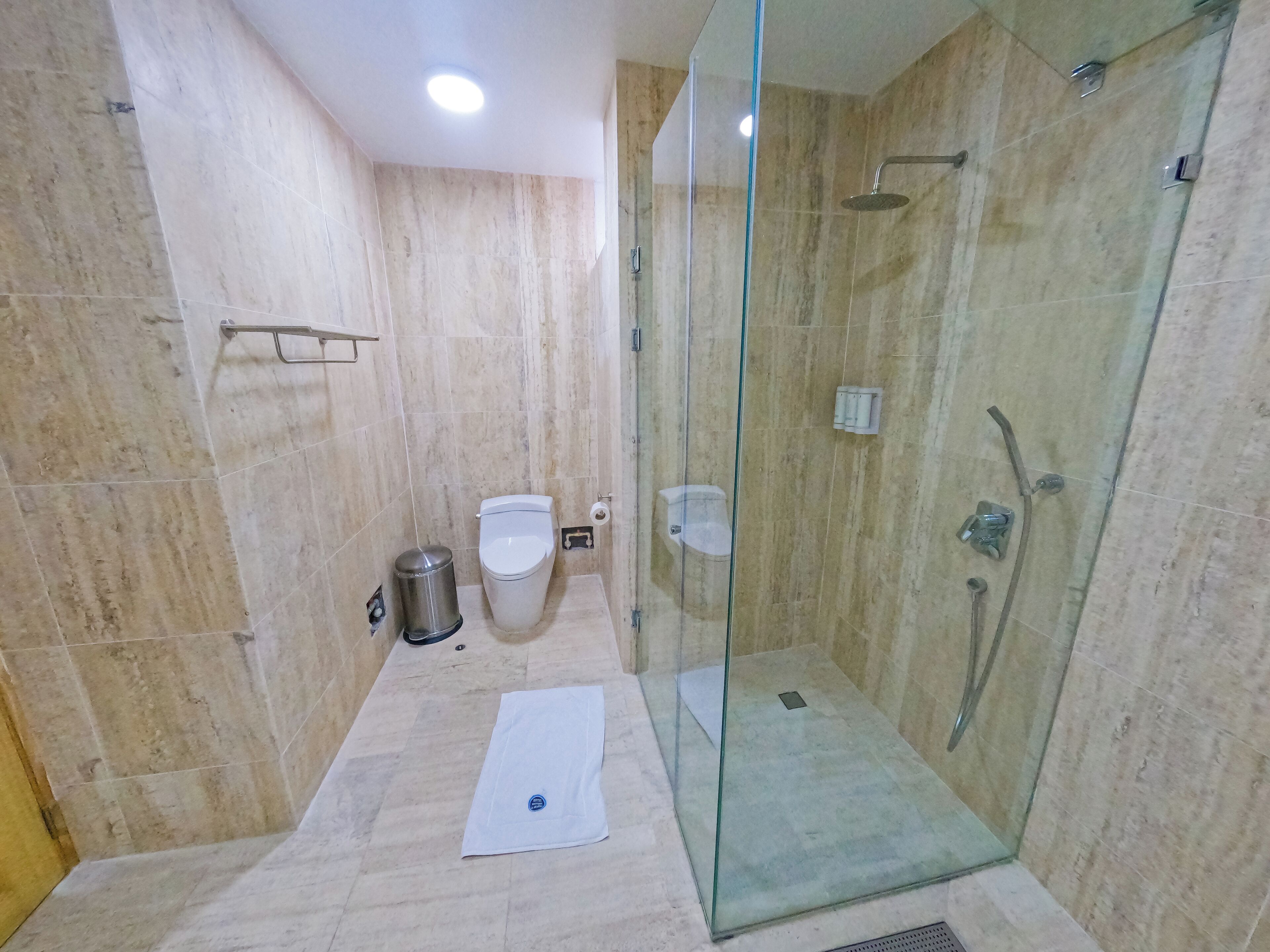 Un baño moderno con ducha envuelta en vidrio, inodoro y un cubo de basura.