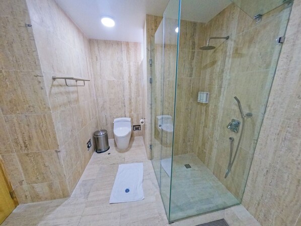 Un baño moderno con ducha envuelta en vidrio, inodoro y un cubo de basura.